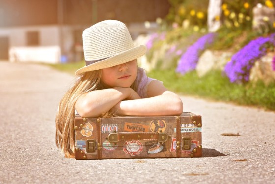 帽子をかぶった女の子が荷物のカバンに組んだ腕を置いている